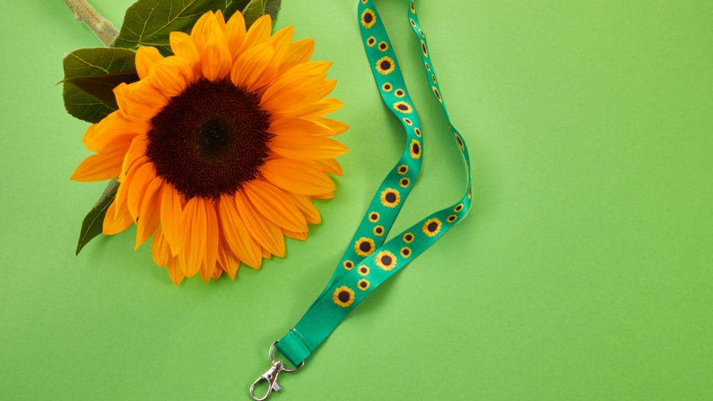 A bright sunflower placed on a green background next to a sunflower lanyard.