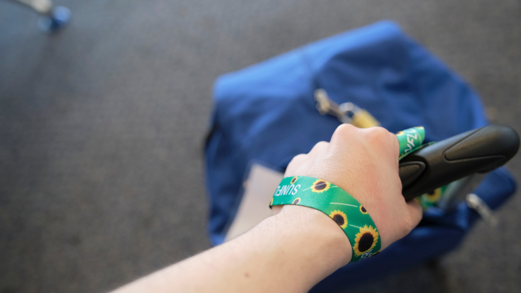 Close-up of a hand holding luggage with a sunflower lanyard attached.