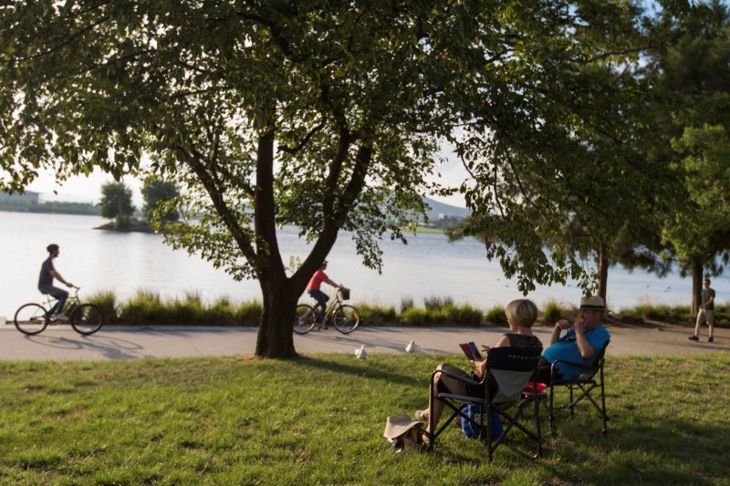 A level shared path runs along the edge of Lake Burley Griffin, with open lawns, trees and the water stretching away towards the city.
