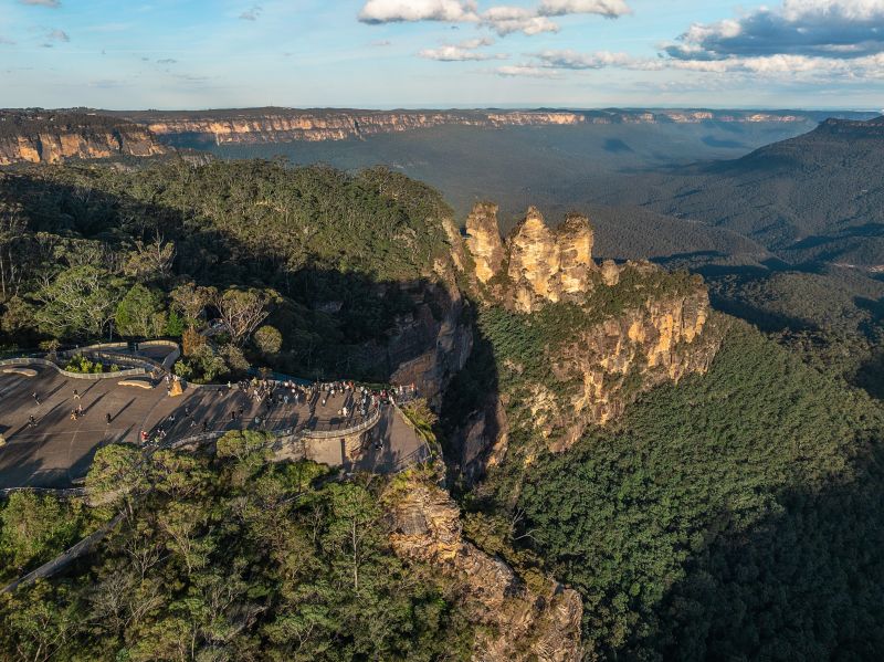 The Three Sisters sandstone formation rises above the forested Jamison Valley in the Blue Mountains, blue haze across the ranges beyond.