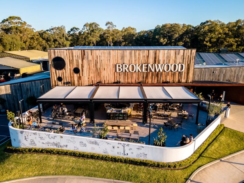 Aerial view of the Brokenwood cellar door in the Hunter Valley, with guests seated under wide awnings on a level terrace surrounded by lawn and bushland.
