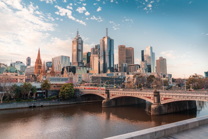 The Melbourne skyline at sunset seen across the Yarra River, with Princes Bridge in the foreground and the spires of Flinders Street and St Paul's beyond.
